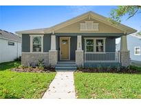 Charming home featuring a covered porch, stone accents, fresh landscaping, and a welcoming yellow front door at 936 57Th N Ave, St Petersburg, FL 33703
