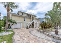 Inviting yellow home with two-car garage, white staircase, and lush tropical landscaping at 633 Soundview Dr, Palm Harbor, FL 34683