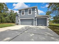Two-story gray home featuring white trim accents and a spacious driveway leading to attached two-car garage at 11257 Persimmon Ave, Weeki Wachee, FL 34614