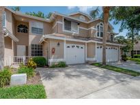 Tan townhome featuring a well-manicured lawn, mature landscaping, and attached one-car garage at 3073 Overlook Pl, Clearwater, FL 33760