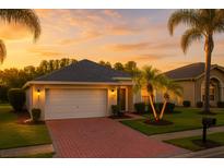 Charming single-story home with a two-car garage, red brick driveway and manicured lawn at sunset at 16113 Rambling Rd, Odessa, FL 33556
