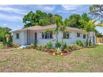 Charming home with manicured lawn and lush landscaping, complemented by young palm trees and vibrant flowerbeds at 1401 49Th N St, St Petersburg, FL 33710