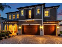 Elegant two-story home featuring a three-car garage and a beautifully lit brick driveway at dusk at 4419 Ortona Ln, Wesley Chapel, FL 33543