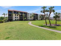 Condominium exterior showing a manicured lawn, mature palms, and a building with multiple screened balconies at 1935 Gulf Of Mexico Dr # G7-304, Longboat Key, FL 34228