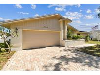 Beige single-Gathering home featuring a two-car garage, driveway with patterned pavers and manicured landscaping at 254 Timberview Dr, Safety Harbor, FL 34695