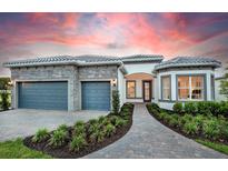 Beautiful home exterior with a lush landscaped yard, stone accents, a gray tiled roof, and a two-car garage at 1845 Ridgemore St, North Port, FL 34289