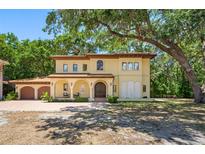 Elegant, two-story Mediterranean-style home with a tile roof and arched entryway, shaded by mature trees at 1966 Freedom Dr, Clearwater, FL 33755