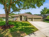Charming single-story home features a well-manicured lawn, mature trees, and a three-car garage at 19808 Sunsplash Ln, Lutz, FL 33558