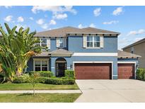 Lovely two-story home painted blue with a three-car garage, elegant entrance, and lush green landscaping at 10017 Smarty Jones Dr, Ruskin, FL 33573