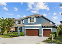 Inviting two-story blue home showcasing a three-car garage and beautifully landscaped front yard under a bright blue sky at 10017 Smarty Jones Dr, Ruskin, FL 33573