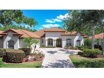 Charming single-story home featuring a tile roof, arched windows, and a brick-paved driveway framed by manicured landscaping at 8474 Dunham Station Dr, Tampa, FL 33647