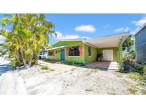 Charming home with a vibrant green exterior, red shutters, blue door, and a covered carport, surrounded by lush trees at 121 86Th Ter, Treasure Island, FL 33706