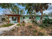 Charming home featuring a light green exterior, wooden pergola and a beautifully landscaped front yard at 3962 Poinsettia Dr, St Pete Beach, FL 33706