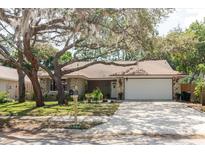 Charming single-story home featuring stone accents, a lush front yard, and mature trees at 7402 America Way, New Port Richey, FL 34654