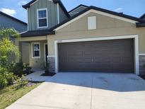 View of the house's garage, siding, stone detail, and driveway with landscaped foliage at 12537 Timber Moss Ln, Riverview, FL 33579