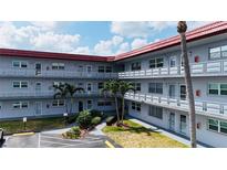 Three story exterior of condo with red roof, multiple balconies, tropical landscaping and dedicated parking at 5660 80Th N St # C101, St Petersburg, FL 33709