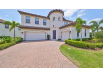 Elegant two-story home featuring a tile roof, manicured landscaping, and a brick-paved driveway leading to a two-car garage at 11909 Climbing Fern Ave, Riverview, FL 33579