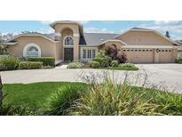 Inviting two-story tan home featuring an arched entryway, a three-car garage, and beautifully landscaped grounds at 16910 Equestrian Trl, Odessa, FL 33556