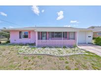 Charming single-story home with a pink exterior, decorative lattice porch, and simple rock garden at 1207 Norwich Cir, Sun City Center, FL 33573