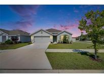 Charming single-story home featuring a well-manicured lawn and a two car garage with a beautiful twilight sky at 2805 Gumbo Limbo Dr, Wimauma, FL 33598
