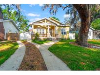 Charming yellow home with a large tree, manicured lawn, and welcoming front porch at 5804 N 9Th St, Tampa, FL 33604