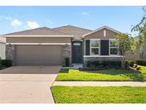 Charming single-story home with a two-car garage, stone accents, and lush landscaping at 13227 Waterleaf Garden Cir, Riverview, FL 33579