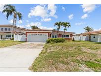 Charming coral home with a well-manicured lawn, attached garage, and beautiful blue skies at 543 Crystal Dr, Madeira Beach, FL 33708