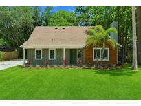 Charming single-story home boasts a lush green lawn, palm tree, and inviting front porch at 7208 N Ola Ave, Tampa, FL 33604