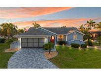 Charming blue single-story home with a red front door, manicured lawn, and a patterned concrete driveway at 220 Singapore Rd, Punta Gorda, FL 33950