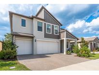 Two-story home featuring a three-car garage, modern facade and a brick-paved driveway and walkway at 21590 Violet Periwinkle Dr, Land O Lakes, FL 34637