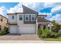 Two-story home featuring a paved driveway leading to a two-car garage, landscaped yard, and modern architectural details at 21590 Violet Periwinkle Dr, Land O Lakes, FL 34637