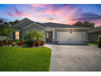 Charming single-story home featuring a well-manicured lawn and a paver driveway beneath a vibrant sunset at 13013 Satin Lily Dr, Riverview, FL 33579