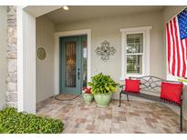 Welcoming front porch features a decorative door, brick pavers, and comfortable bench seating with vibrant red pillows at 4220 Barletta Ct, Wesley Chapel, FL 33543