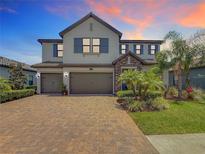 Two-story home featuring a three-car garage, well-manicured lawn, brick paver driveway, and stone accents at 18203 Pine Hammock Blvd, Lutz, FL 33548