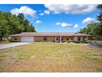 Charming single-story red brick home featuring an attached two-car garage and manicured landscaping at 11514 Sun Rd, Dade City, FL 33525