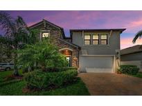 Charming home featuring stone accents, manicured landscaping, brick paved driveway, and a two-car garage at twilight at 2653 Longleaf Pine Pt, New Port Richey, FL 34655