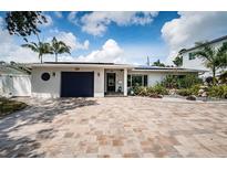 Charming home featuring a paver driveway, manicured landscaping, a blue garage door, and neutral exterior paint at 333 Belleair Ne Dr, St Petersburg, FL 33704