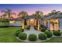 Elegant home featuring manicured landscaping, a circular driveway, and a covered entryway, set against a colorful dusk sky at 10117 Breezy Pines Ct, Weeki Wachee, FL 34613