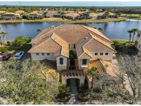 Aerial view of a waterfront condo with a clay tile roof, lush landscaping, and serene lake views at 1348 Emerald Dunes Dr, Sun City Center, FL 33573