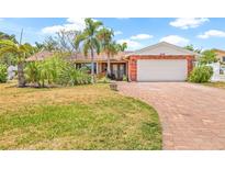 Charming single-story brick home featuring a two-car garage, red brick driveway, and tropical landscaping at 1141 80Th Street S Ct, St Petersburg, FL 33707