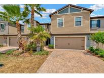 Inviting two-story townhouse with a brick-paved driveway, attached garage, and lush landscaping with palm trees at 28516 Tranquil Lake Cir, Wesley Chapel, FL 33543