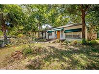 Charming home with mature landscaping, a cozy front porch and a cheerful yellow door at 1211 E Park Cir, Tampa, FL 33604