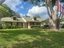 Charming single-story home with dormer windows, a lush lawn, mature trees, and well-maintained landscaping at 8361 Cofield Ln, Spring Hill, FL 34608
