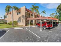 Condo exterior with parking, red roof, beige walls, mature landscaping, and palm trees under a sunny sky at 120 Cedarwood Cir # 120, Seminole, FL 33777