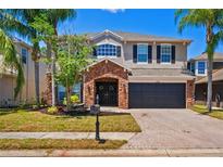 Charming two-story home featuring a stone-accented entry, dark-stained garage door, and palm tree-lined front yard at 12935 Solola Way, Trinity, FL 34655