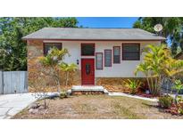 Charming home featuring a stone facade, bright red door, and tropical landscaping at 705 Cypress St, Tarpon Springs, FL 34689