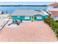 Waterfront home featuring a bright blue exterior, lush landscaping, and a brick paved driveway at 326 176Th Avenue Cir, Redington Shores, FL 33708