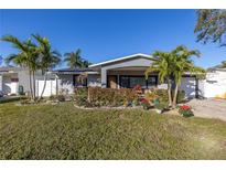 Charming single-story home with a well-manicured lawn and lush landscaping, including palm trees at 1990 59Th N St, St Petersburg, FL 33710