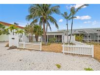 Charming home featuring a white picket fence, gravel yard, and mature tropical landscaping with palm trees at 101 11Th Ave, St Pete Beach, FL 33706