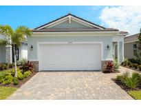 Charming home featuring a two-car garage, lush landscaping, and a brick-paved driveway at 11359 Boundless Ter, Venice, FL 34293